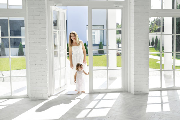 快乐的妈妈和宝宝从后院走进屋子。这家人正在检查公寓，准备购买房地产。有大窗户的房间母亲和孩子穿着优雅的白裙子图片下载