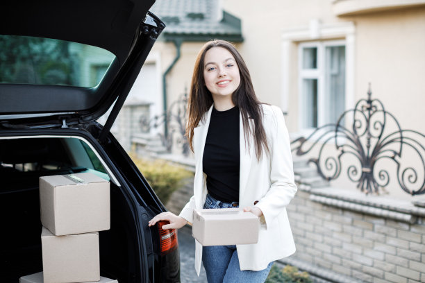 年轻的女商人从汽车后备箱里捡包裹，开车回家。网上购物并送货回家的概念图片下载