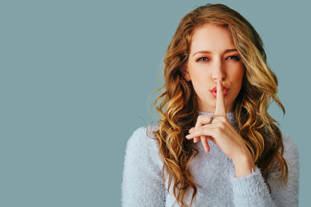 一个美丽的年轻女人的肖像，长卷发，穿着毛衣，手指上嘴唇秘密hush图片下载