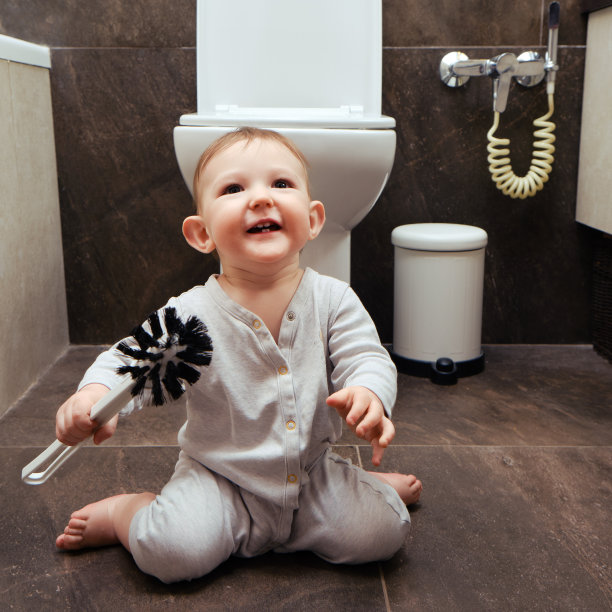 快乐的蹒跚学步的小男孩正在厕所里玩刷子。一个微笑的孩子在米色浴室的棕色地板上玩耍图片下载