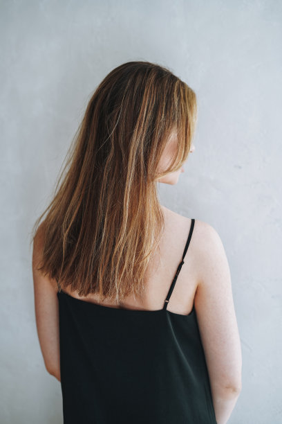 年轻女子的肖像与晚上优雅的黑色长裙从背部在白色的内饰图片下载