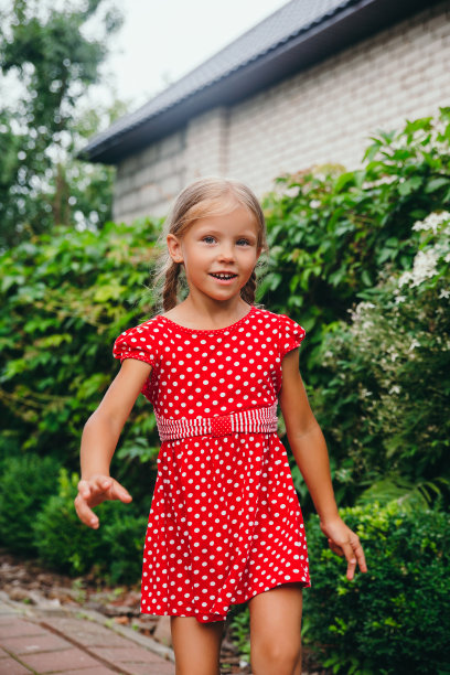 快乐的小女孩穿着红裙子，扎着辫子在花园里散步。暑假。图片下载