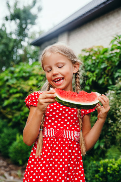 小女孩穿着红裙子在花园里吃西瓜。图片下载