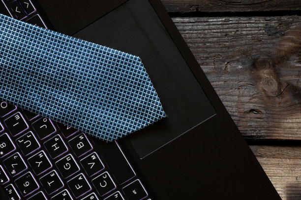 一条蓝领带躺在家里木桌上的黑色笔记本电脑上，在网上工作图片下载