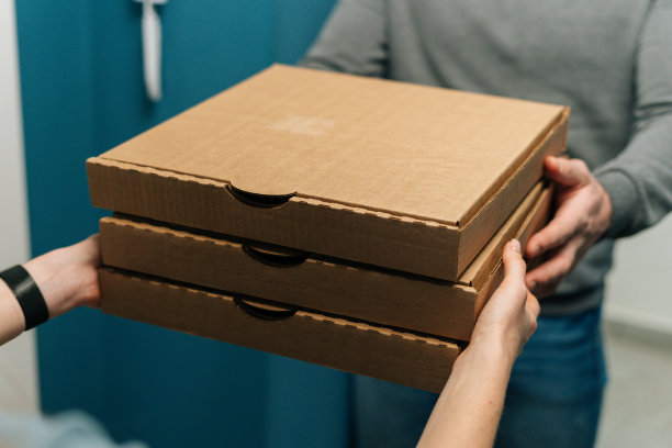 特写镜头的不知名的女性客户接收纸箱的披萨在家里从送货员的手。图片下载