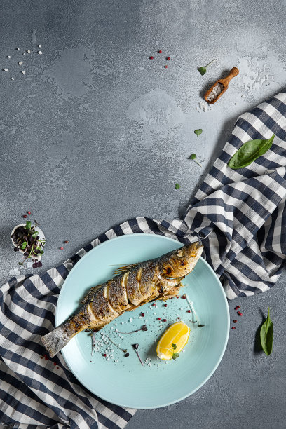 蓝色板烤鲈鱼，石材背景与纺织品。烤鱼在餐厅的菜单概念。柠檬烤虹鳟鱼。当代海鲜菜单。地中海食物。图片下载