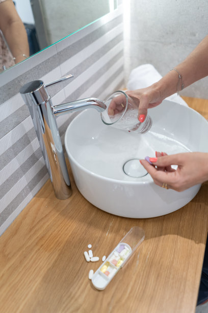 一个女人手里拿着一杯水吃头痛药。图片下载