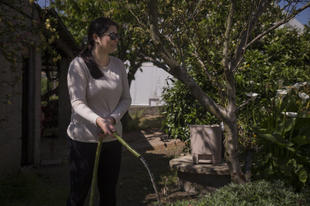 成熟的女人戴着太阳镜在花园里浇水。图片下载
