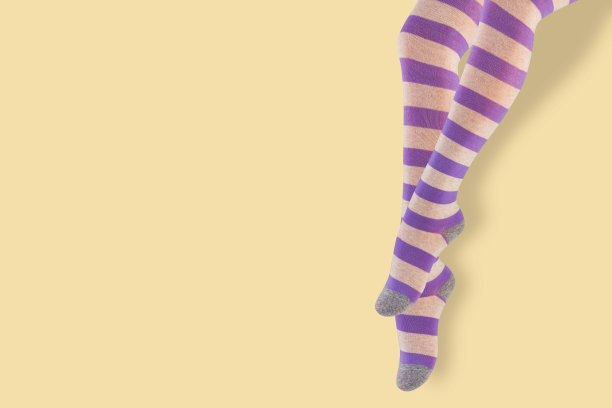 女性下垂的腿，穿着淡紫色条纹的连裤袜，黄色背景，概念图片下载