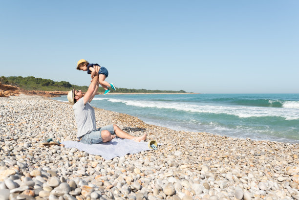 父亲抱着她的小女儿在地中海的海滩上。图片下载