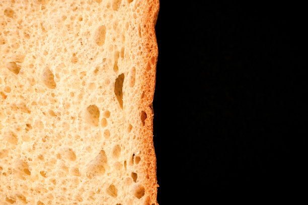 一片白面包在黑色背景上孤立地靠近。粗糙的斑点表面纹理切块面包天然有机食品与孔。前视图。行星和空间的抽象概念图片下载