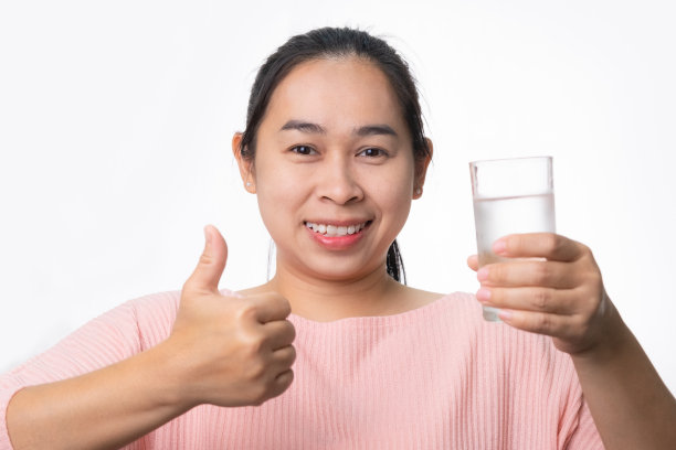 微笑的女人拿着一杯水和大拇指在演播室的白色背景。健康的生活方式图片下载