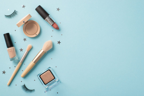 化妆美容的概念。俯视图照片的假睫毛，口红，化妆刷，眼影，指甲油和星形彩纸上孤立粉彩蓝色背景与空白空间图片下载