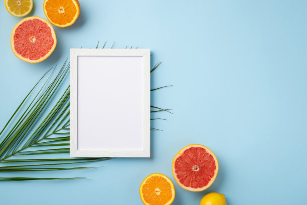 暑假的概念。俯视照片的白色相框和成熟的热带水果切柠檬橙子柚子和棕榈叶孤立粉彩蓝色背景与空白图片下载
