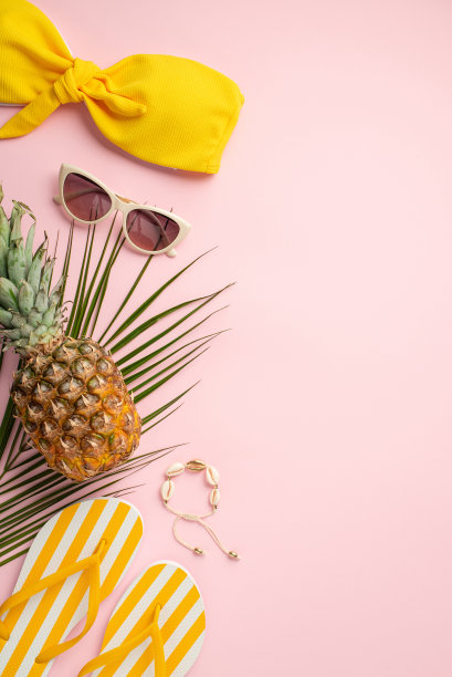 暑假的概念。俯视图垂直照片黄色泳装紧身胸衣太阳镜黄色条纹拖鞋菠萝壳手镯和棕榈叶孤立粉彩背景图片下载