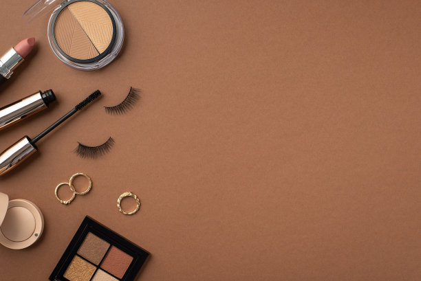 化妆美容的概念。俯视图照片的轮廓和眼影调色板假睫毛睫毛膏金戒指和口红在孤立的棕色背景与copyspace图片下载