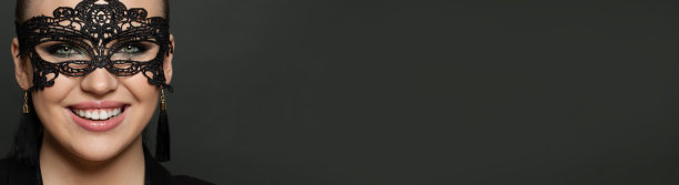 狂欢节面具特写美丽女人的脸。快乐的女人戴着狂欢节面具在黑暗的旗帜背景图片下载