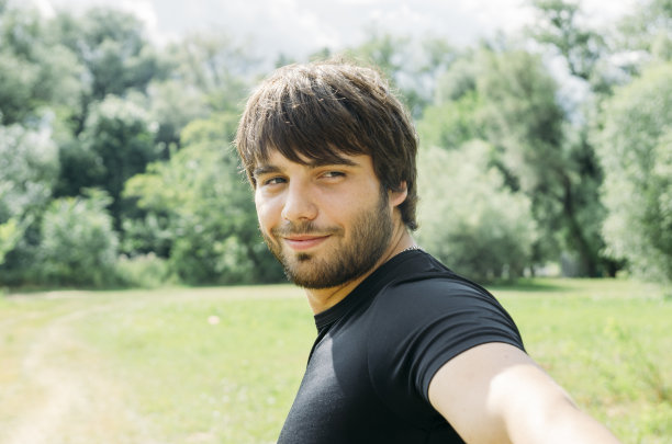 年轻英俊男子的肖像，拿着相机和户外自拍与智能手机。图片下载