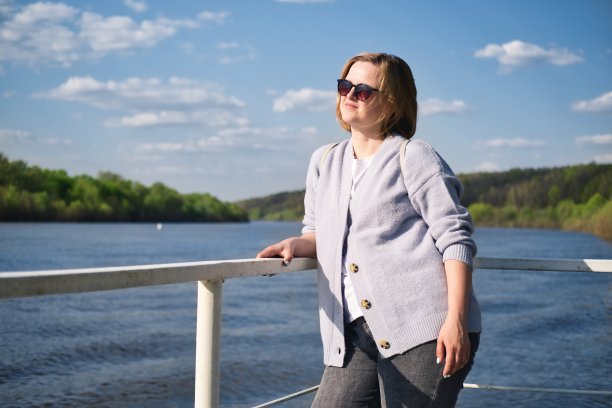 在温暖的夏天阳光明媚的一天，迷人的白种女人戴着太阳镜在河边的码头上摆姿势的肖像。图片下载