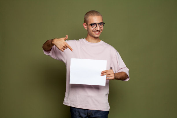 有吸引力的开朗的年轻人拿着白色的空纸板和微笑在绿色的背景图片下载