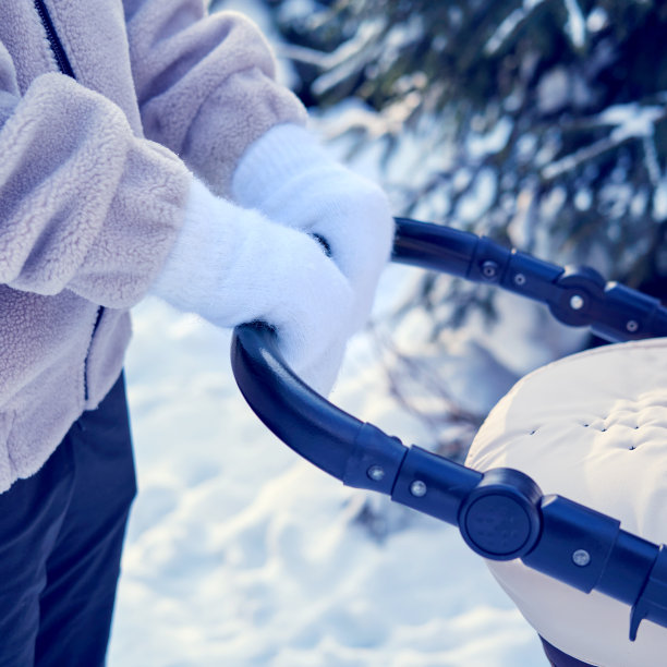 妇女母亲与婴儿车的一个孩子在冬季公园附近白雪覆盖的圣诞树。妈妈推着婴儿车，在树林里的积雪中穿行图片下载