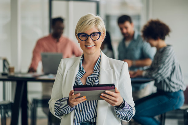 一位女商人站在办公室里的肖像，同事们在后面图片下载