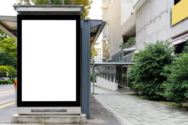 广告牌模拟在城市背景美丽的阳光。模板一个空信息广告牌附近的车站的公共交通，模型的城市旗帜占位符和海报。图片下载