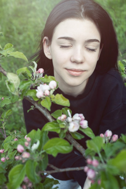 漂亮的十几岁的女孩在花园附近花苹果树粉红色的花摆姿势。图片下载