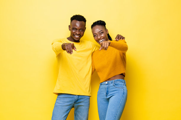年轻快乐的非洲夫妇指着相机上孤立的黄色演播室背景图片下载