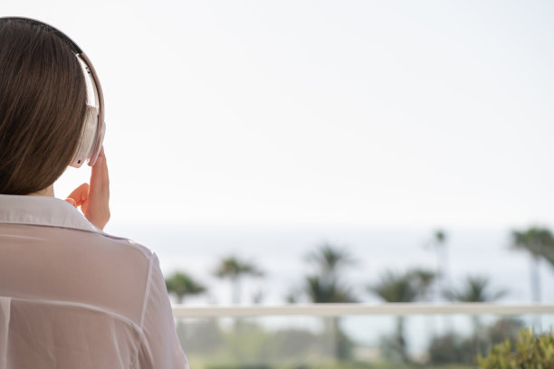 后视图的女人与耳机看棕榈树，海滩在日落。女性在放松地听音乐。图片下载