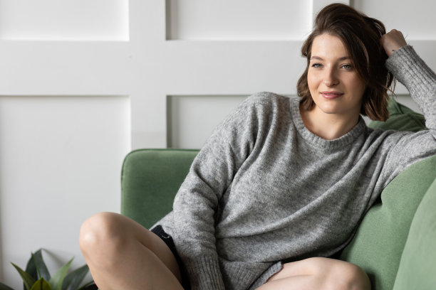 美丽的年轻女子在家里客厅的沙发上放松。日光。女性在灰色毛衣填充舒适在她的房子。周末图片下载