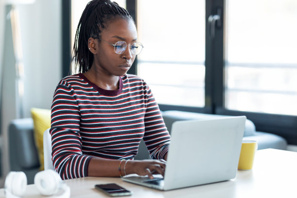 美丽年轻的非洲女商人工作与笔记本电脑坐在家里的办公室。图片下载