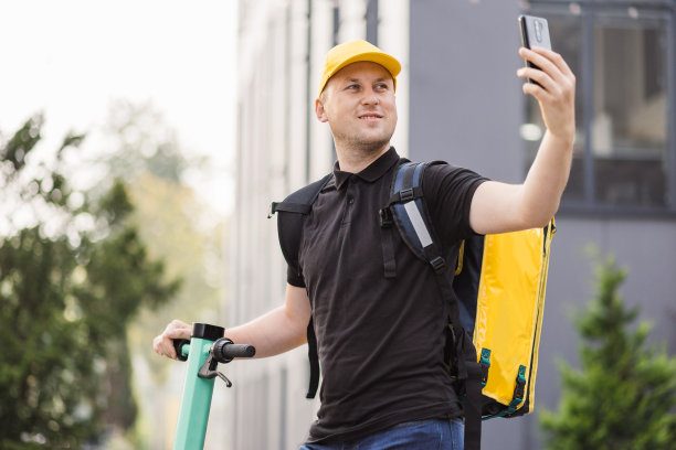 带着黄色热背包的快递员背着电动滑板车走在街上图片下载