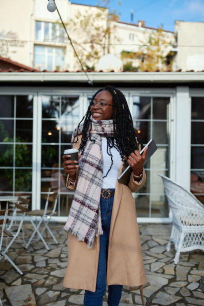 一个自由职业者走在咖啡馆前面，手里拿着咖啡，手里拿着笔记本电脑。图片下载