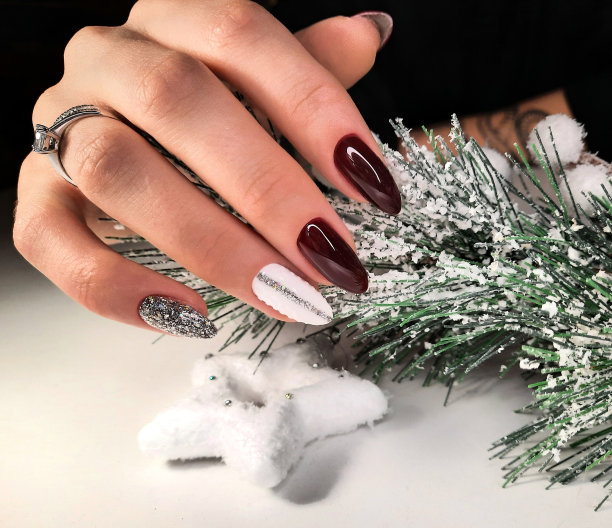 一个整洁的美甲与覆盖着雪的圣诞树树枝。长而圆的指甲上涂着红色的凝胶，白色的设计和银色的闪光图片下载