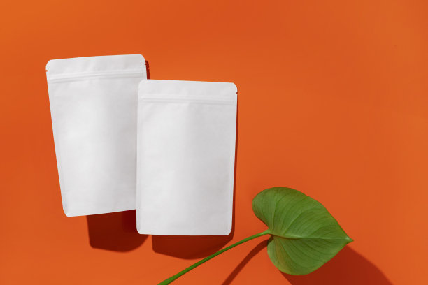 白色纸板包装的茶/咖啡/香料/小吃和monstera叶在橙色的背景。品牌和包装模型。图片下载