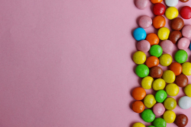 五颜六色的糖果和口香糖。粉红色背景上的彩色糖果。彩色巧克力釉的小糖果。位于右边。巧克力点心。从以上观点。副本的空间。平的。图片下载