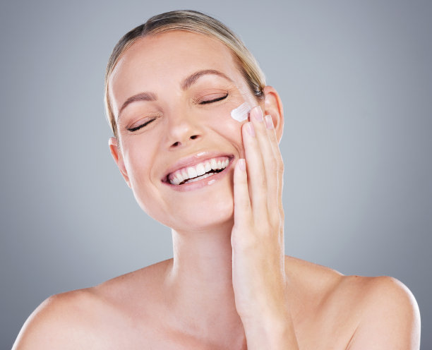 一名迷人的成熟女性在灰色背景下涂抹润肤霜图片下载