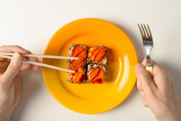 白种人手拿筷子和叉子，在盘子里放着热烤面包卷，这是传统的日本食物。亚洲美食的选择和方便的概念。顶视图,特写图片下载