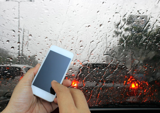 手拿着智能手机，透过车窗看路面上的雨滴图片下载