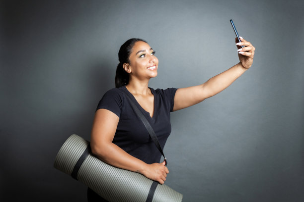 运动西班牙年轻女子与瑜伽垫与智能手机视频通话图片下载