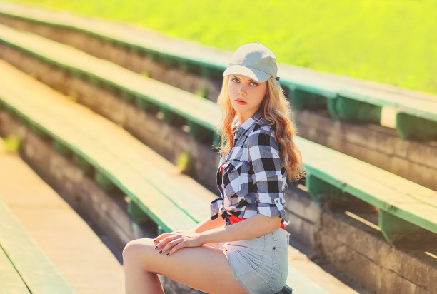 美丽的年轻金发女子的肖像戴着棒球帽，短裤和衬衫在夏天的公园图片下载