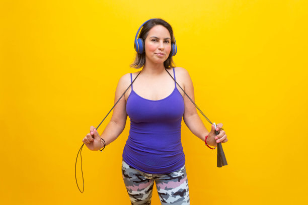 中年成熟女子穿着运动服和耳机，站着抱跳绳图片下载