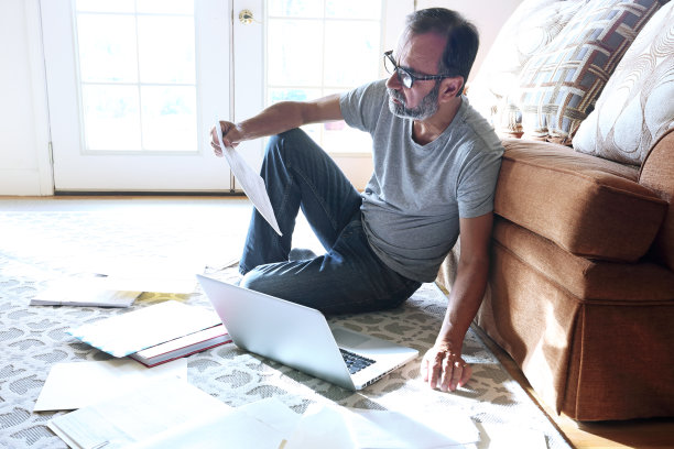 拉丁裔男子坐在地板上靠在沙发上在家工作图片下载