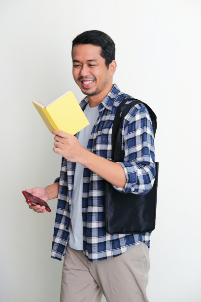 成年亚洲男子散步放松，并显示快乐的表情，同时阅读一本书图片下载