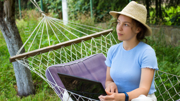 有思想的年轻女子戴着夏天的帽子，使用笔记本电脑，坐在绿色花园的吊床上，看着一边。分心沉思的女孩思考任务，思考决定在周末，假期远程工作图片下载