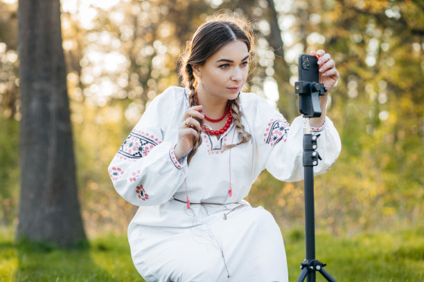 乌克兰年轻部落客女孩身着民族服装，在森林中旅行时用手机拍摄视频图片下载