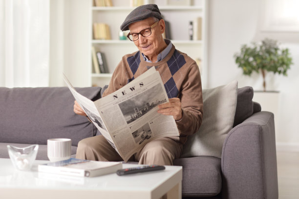 一位老人坐在家里的沙发上看报纸图片下载