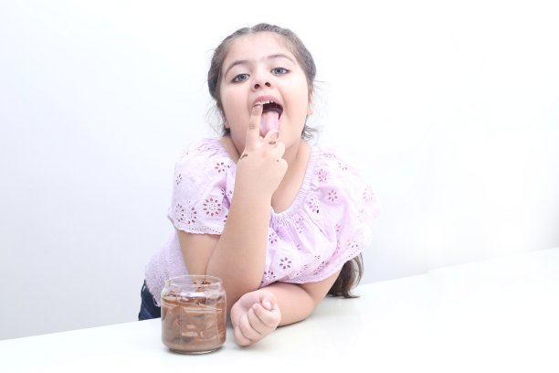 印度小女孩用手指吃罐子里的巧克力酱图片下载