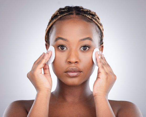 年轻女子在灰色背景前用棉花擦脸的影棚照片图片下载